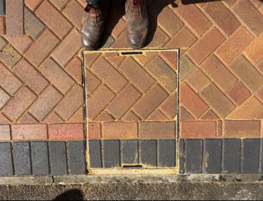 Manhole cover neatly finished flush within herringbone block paving during driveway installation