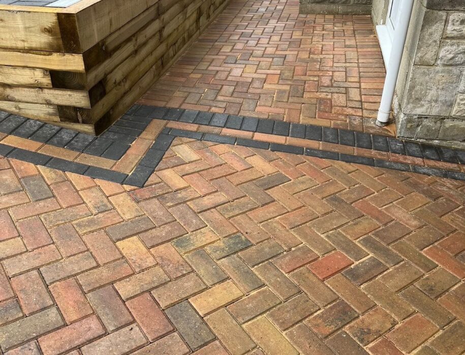 Close-up of herringbone block paving pathway alongside a timber sleeper retaining wall and raised planter