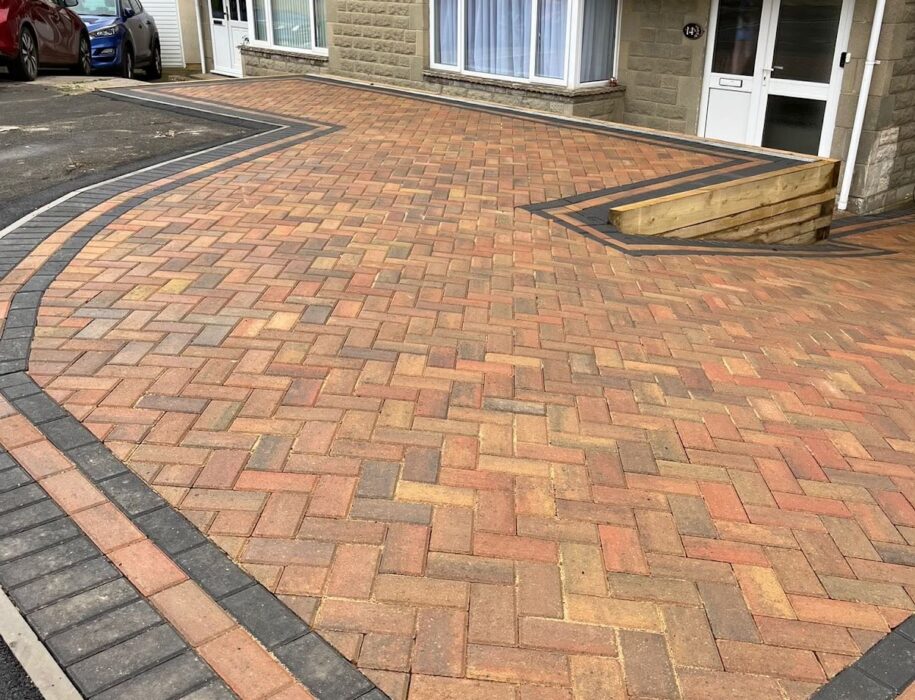 Completed curved herringbone block paving driveway with charcoal border and timber sleeper retaining wall, Wiltshire