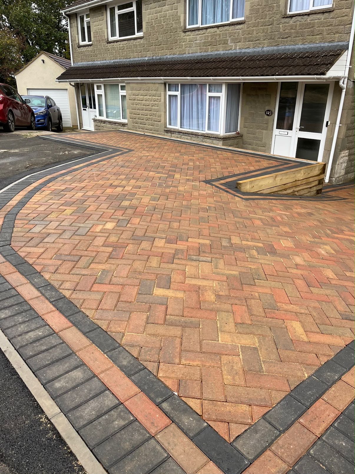 Completed curved herringbone block paving driveway with charcoal border and timber sleeper retaining wall, Wiltshire