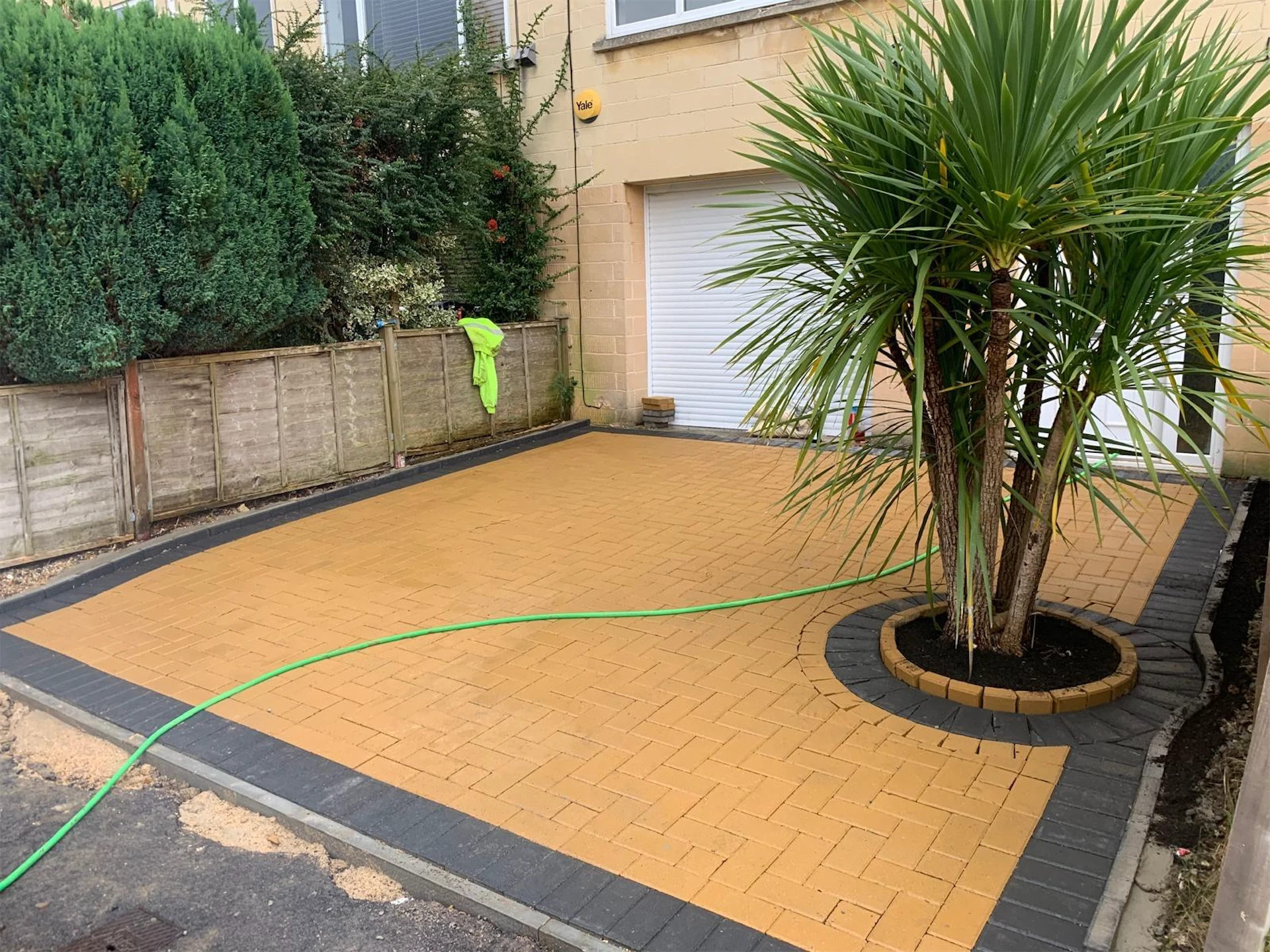 Orange herringbone block paving driveway with a charcoal edging border and a circular planter around a palm tree