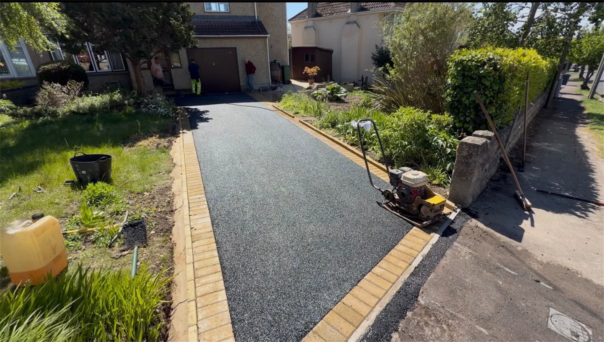 Smooth black tarmac driveway with brindle brick border edging, leading to a house garage