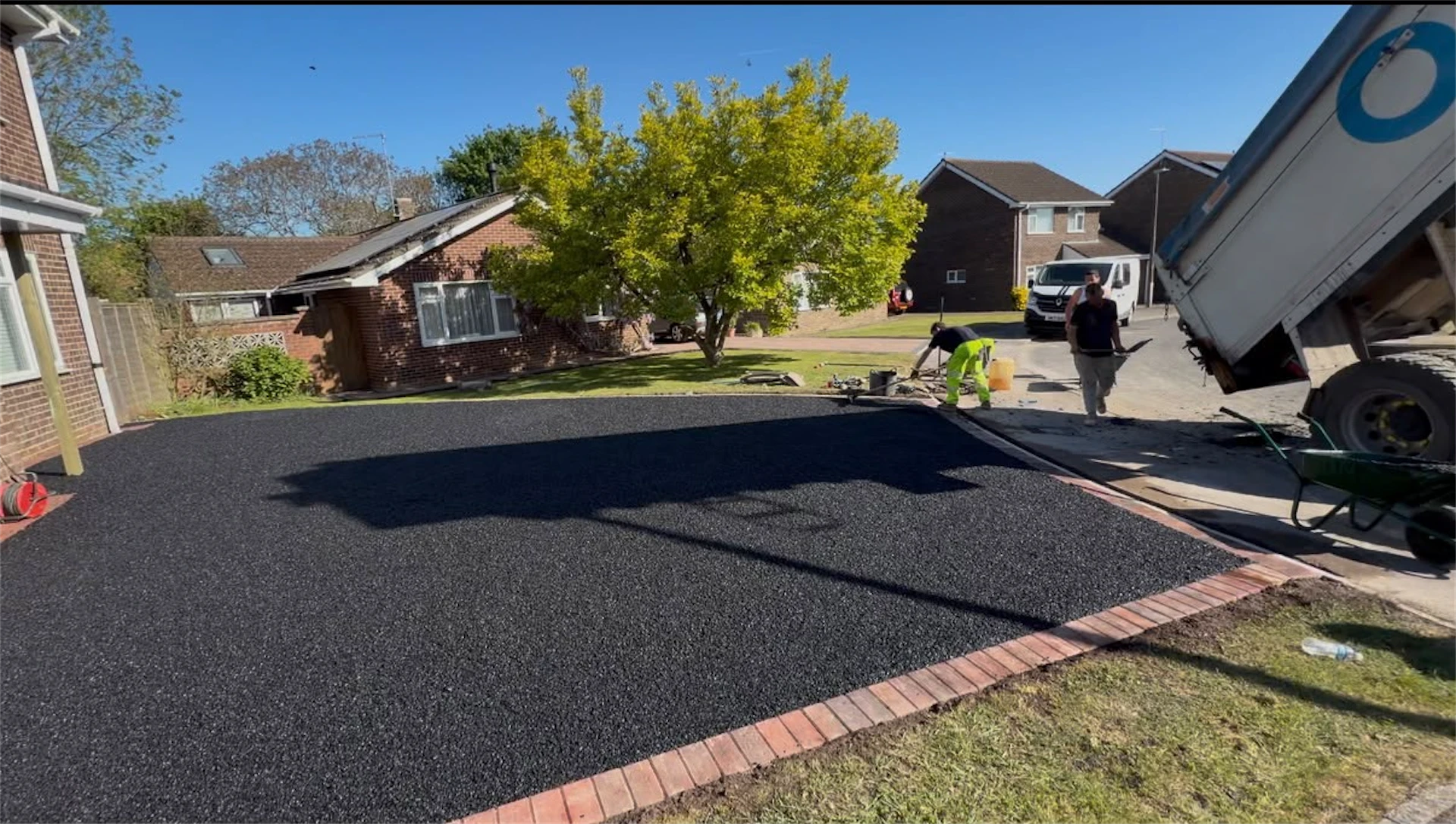 Freshly laid black tarmac driveway with a red brick edging border, tipper truck delivering materials